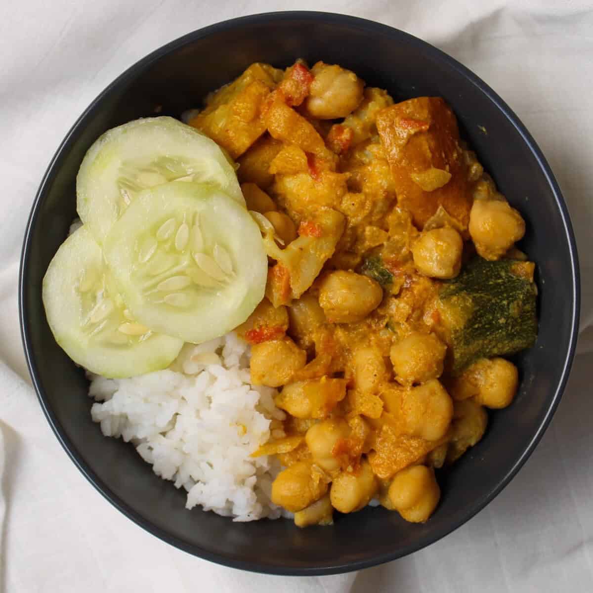 Bowl of rice and chickpea curry topped with cucumber slices.