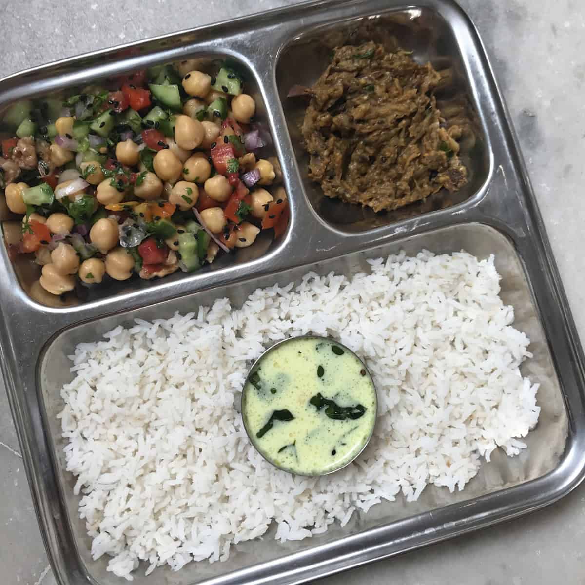 Chickpea salad, vankaya pachadi, kadhi, and rice on a steel plate.