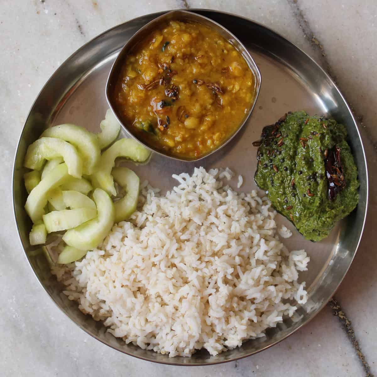Indian lunch plate with rice, dal, spinach chutney, and sliced cucumber.