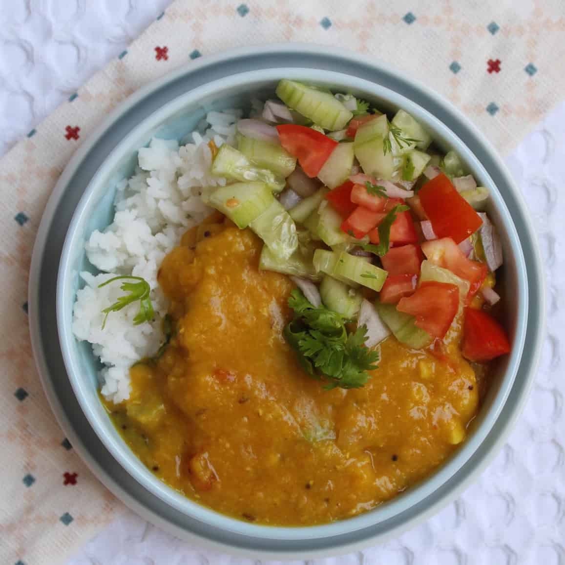Rice bowl topped with red lentil dal and served with cucumber, onion, and tomato salad.