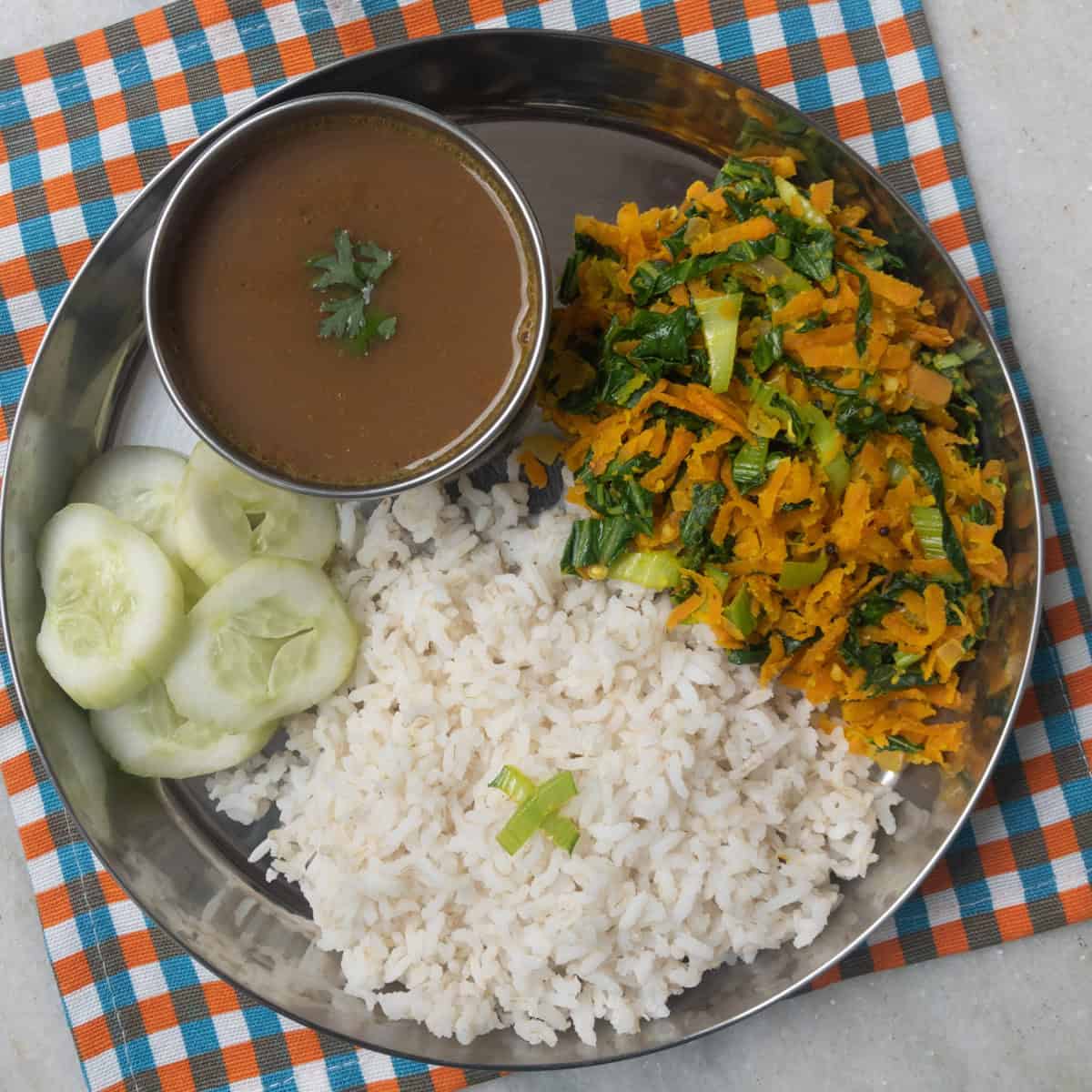 South Indian lunch plate with rice, carrot stir fry, cucumber slices, and ulavacharu served on a stainless steel plate.