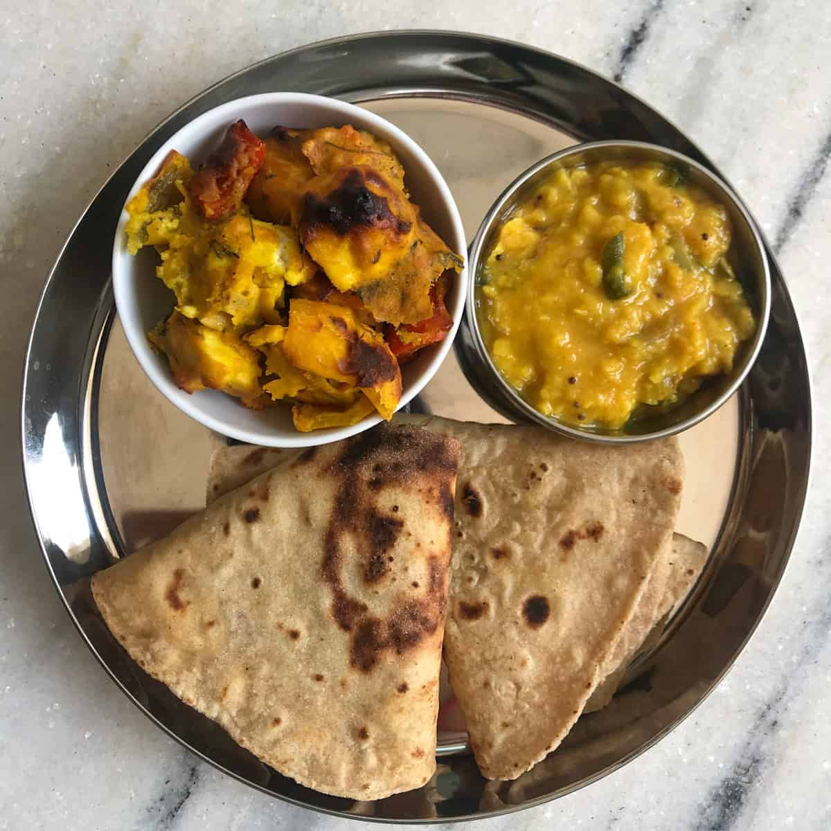 Indian lunch plate with roti, dal, and roasted paneer and vegetables in a bowl.