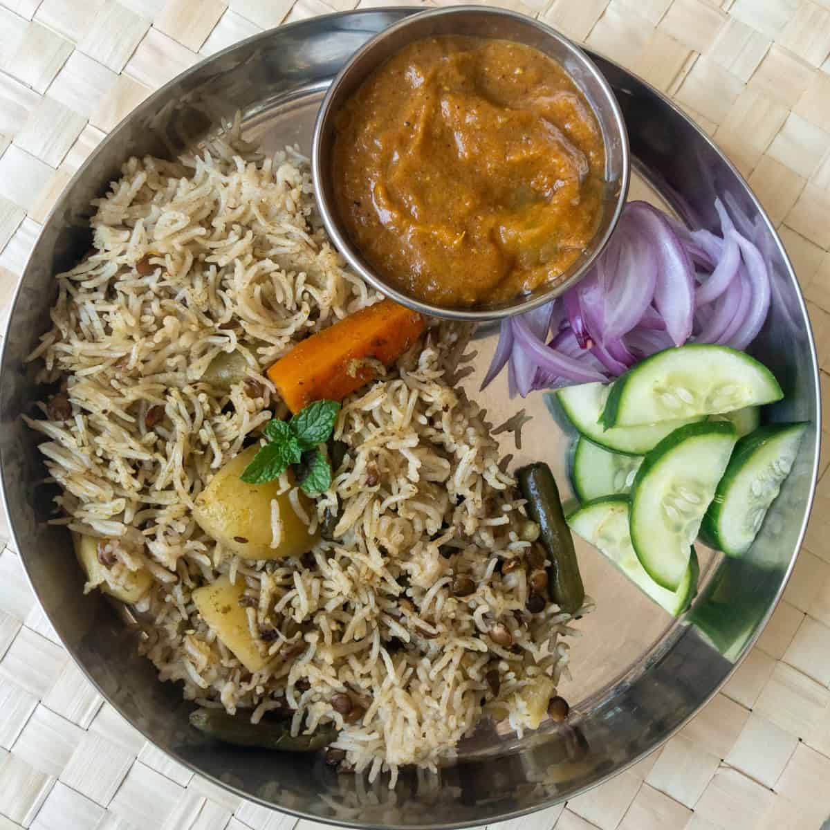 Indian lunch plate with vegetable pulao, mixed veggie curry, cucumber, and onion salad.