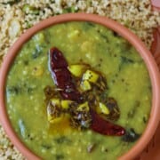 A bowl of gongura pappu topped with tempering of dried red chilies and spices, served on a plate with cooked millet.