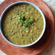 A bowl of mixed dal tadka garnished with fresh cilantro, served on a decorative clay plate.