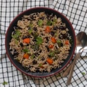A bowl of mixed vegetable black beans basmati rice garnished with fresh cilantro, placed on a black and white checkered cloth with a spoon and fork beside it.