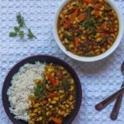 A bowl and a plate of Black-Eyed Peas Curry served with rice on a white textured background.
