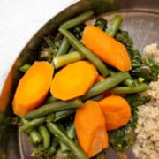 Close-up of steamed green beans and sliced carrots atop saag on a stainless steel plate, next to quinoa, with 'Everyday Nourishing Foods' watermark.