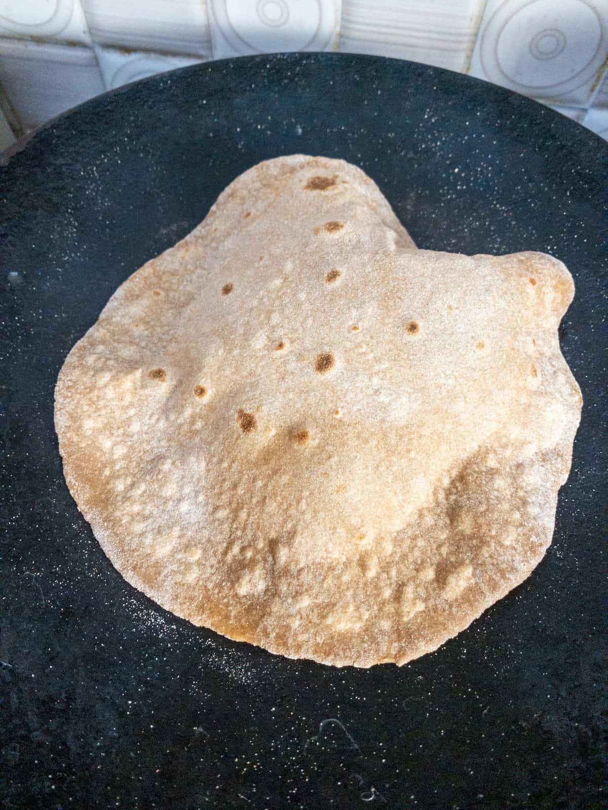 Fully puffed chapati on a tawa, cooked evenly with golden spots.