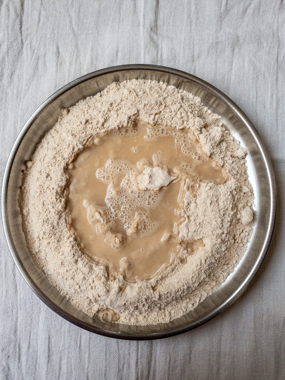 Water poured into the center of whole wheat flour in a steel plate for making Indian bread dough.