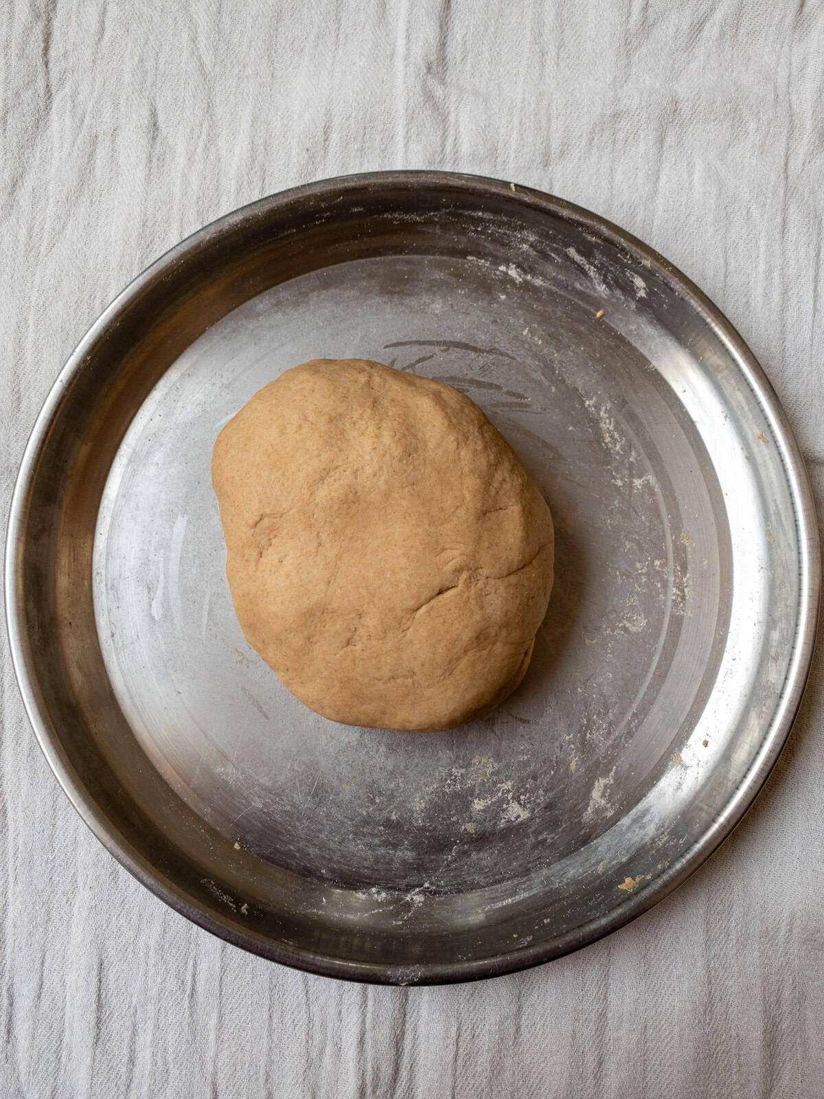 Smooth and well-kneaded Indian bread dough resting in a steel plate before rolling.