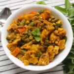 A bowl of Indian vegetable side dish - veggie curry garnished with fresh mint, served with a side of curry leaves on a striped napkin.