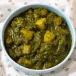 A bowl of Saag Aloo – Indian spinach and potato curry – served in a light blue bowl, showing chunky potatoes coated in a vibrant green spinach gravy.