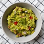 Bowl of Indian-style spicy guacamole topped with green chili slices and herbs.