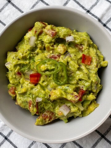 Bowl of Indian-style spicy guacamole topped with green chili slices and herbs.