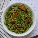 Bright and colorful palak pulao served in a white bowl, showing the contrast of green spinach rice and orange carrot pieces, styled on a striped towel.