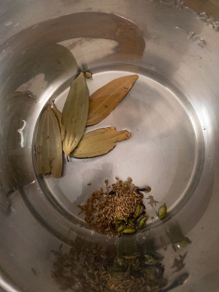 Bay leaves, cumin seeds, cloves, and cardamom warming in the stainless steel Instant Pot insert.