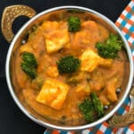 Close-up of broccoli paneer curry in a brass-handled serving bowl, showing golden paneer cubes and broccoli florets in a spiced tomato gravy.