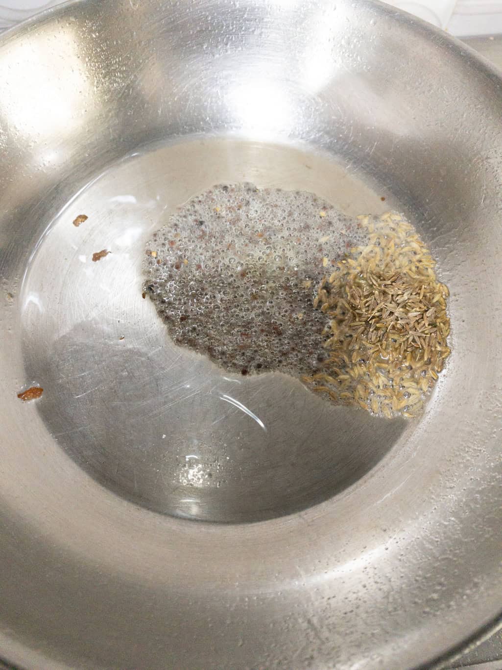 Mustard seeds and cumin seeds sizzling in hot oil in a stainless steel pan for lemon rice tempering.