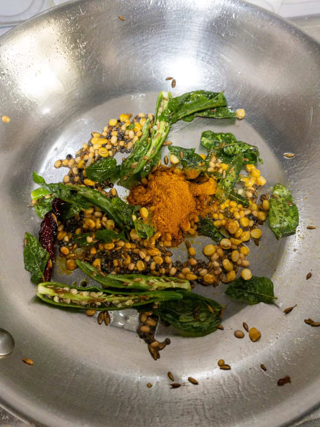 Bright yellow turmeric powder added to the hot tempering of dals, curry leaves, and chilies in a stainless steel pan.