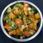 Close-up of spicy Indian tomato onion salad with fresh cilantro, onions, and tomatoes mixed with spices in a small steel bowl.