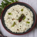 Creamy yogurt rice in a black bowl topped with tempered curry leaves, dried red chili, and black pepper.