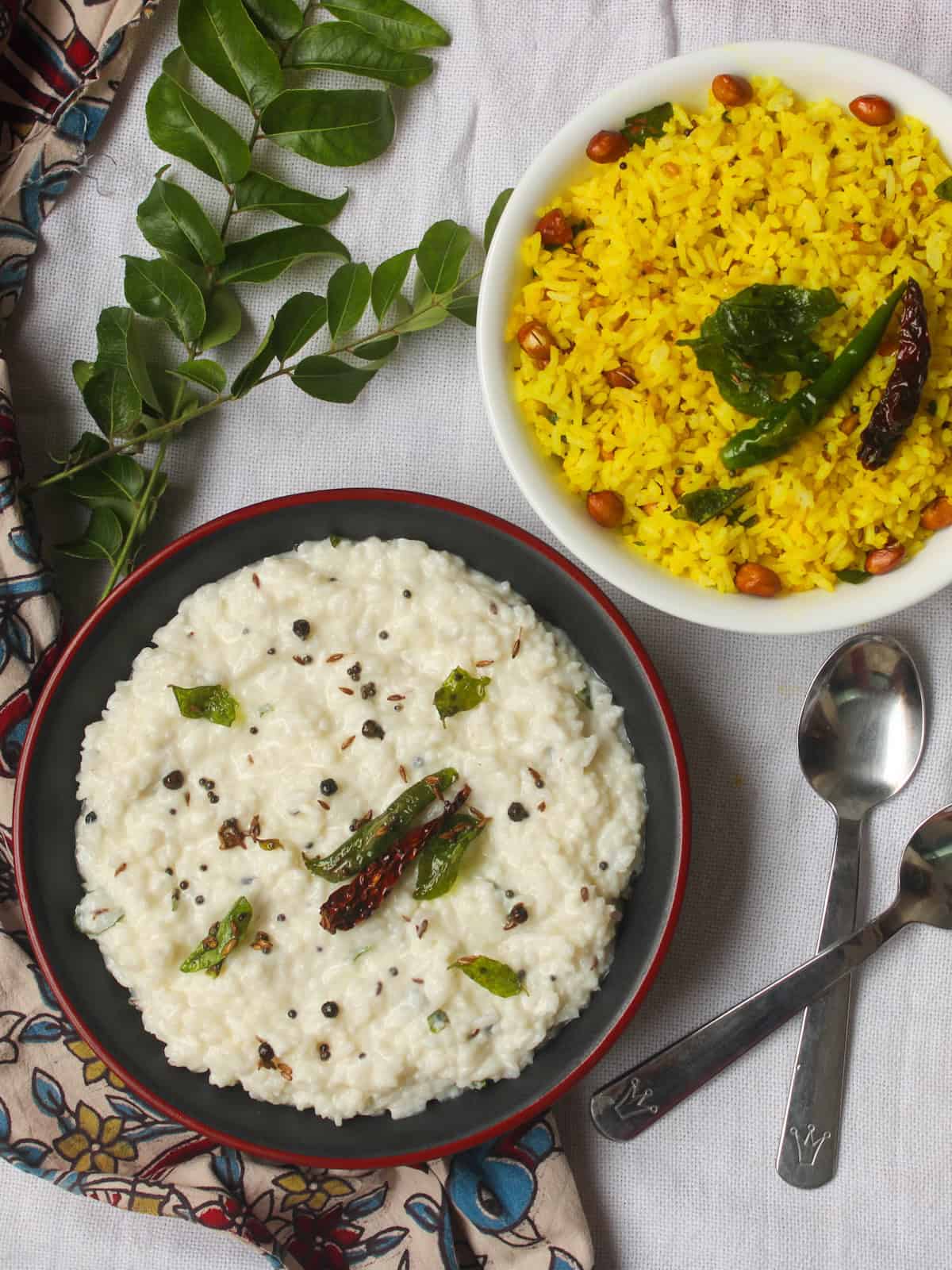 Yogurt rice with tempering served alongside lemon rice in a white bowl, curry leaves in the background, and spoons on the side.