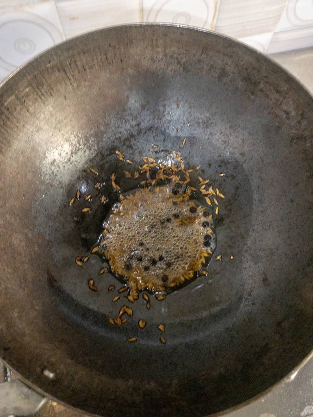 Cumin seeds frying with whole peppercorns in hot oil.