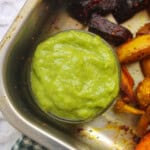 Small glass bowl of creamy avocado cilantro dip placed in a tray with roasted beetroot, potato, and cauliflower.