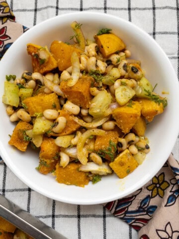 Close-up of black-eyed peas and roasted butternut squash salad in a white bowl placed on a checkered cloth.