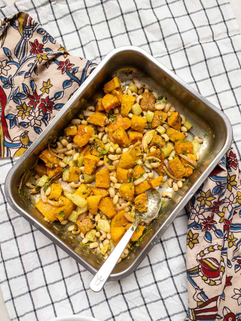 Fully mixed black-eyed peas and roasted squash salad in a steel tray with a serving spoon.