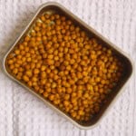 A tray of golden brown Indian spiced roasted chickpeas on a white textured cloth background.