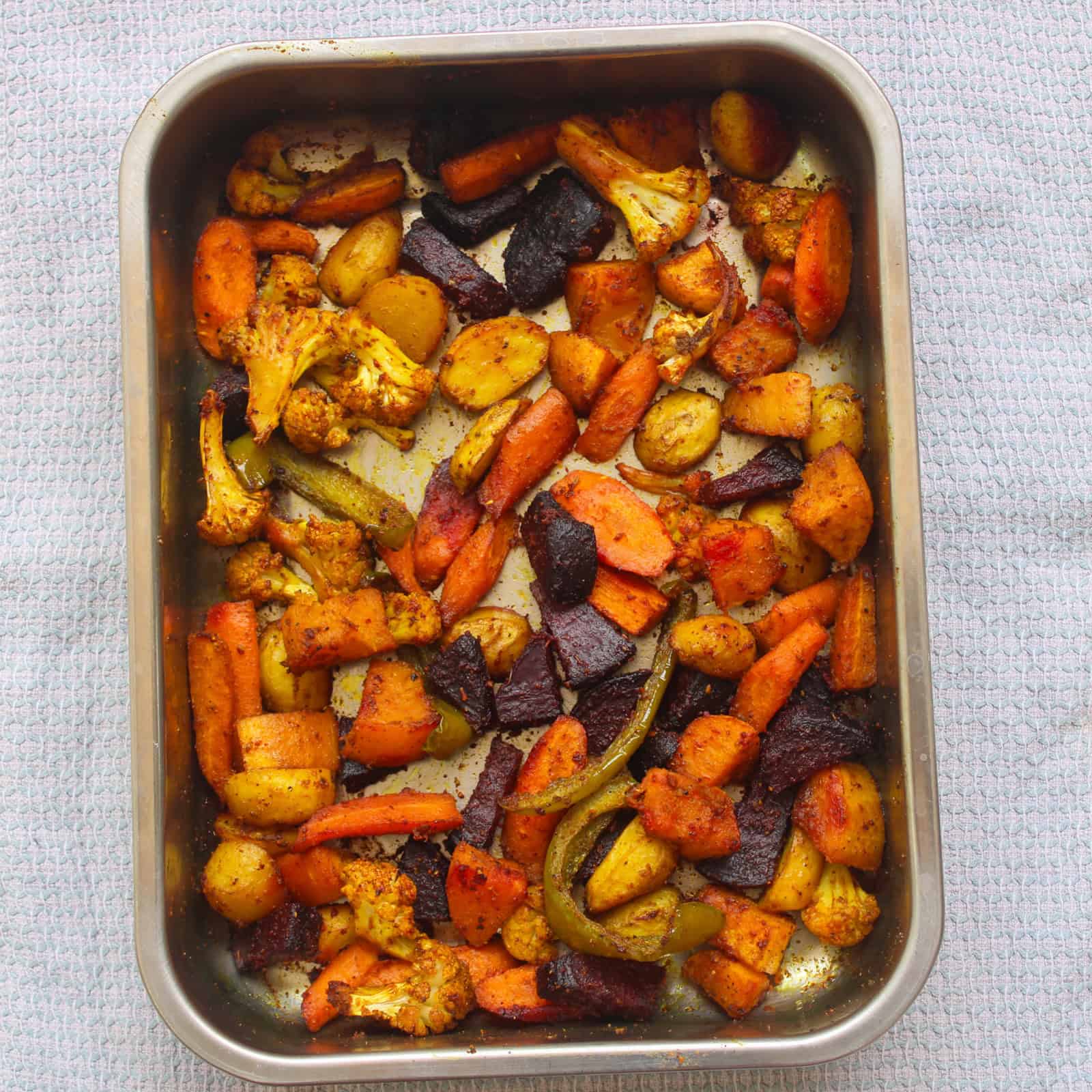 Indian spiced roasted vegetables baked on a tray with golden edges and crispy texture.