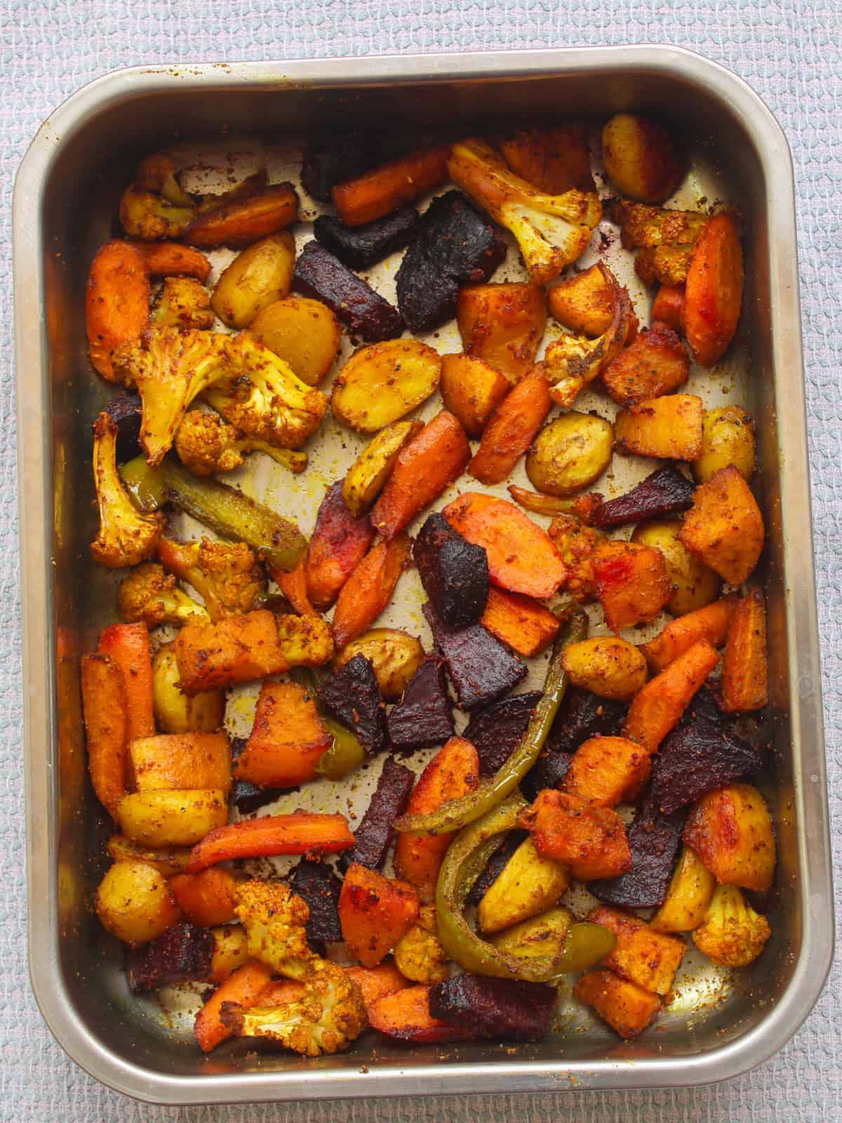 Roasted Indian vegetables in a tray with crispy, caramelized edges after baking.