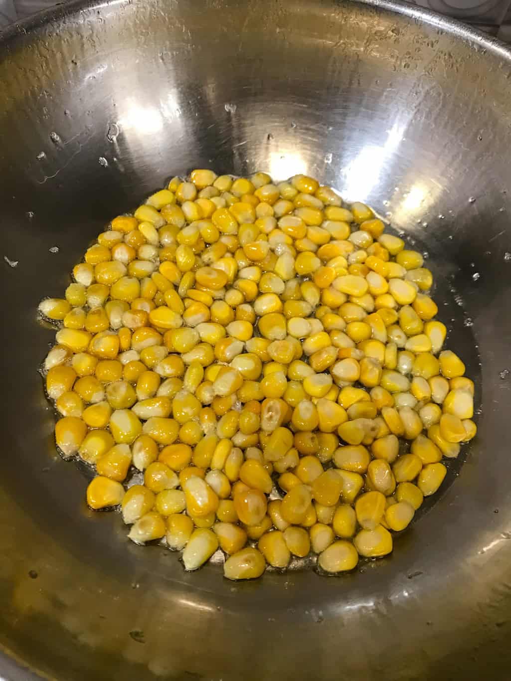Golden sweet corn kernels sautéing in oil in a steel pan.