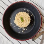 Top view of cooked millet formed into a neat round shape, garnished with basil, placed in a black bowl on a striped cloth.