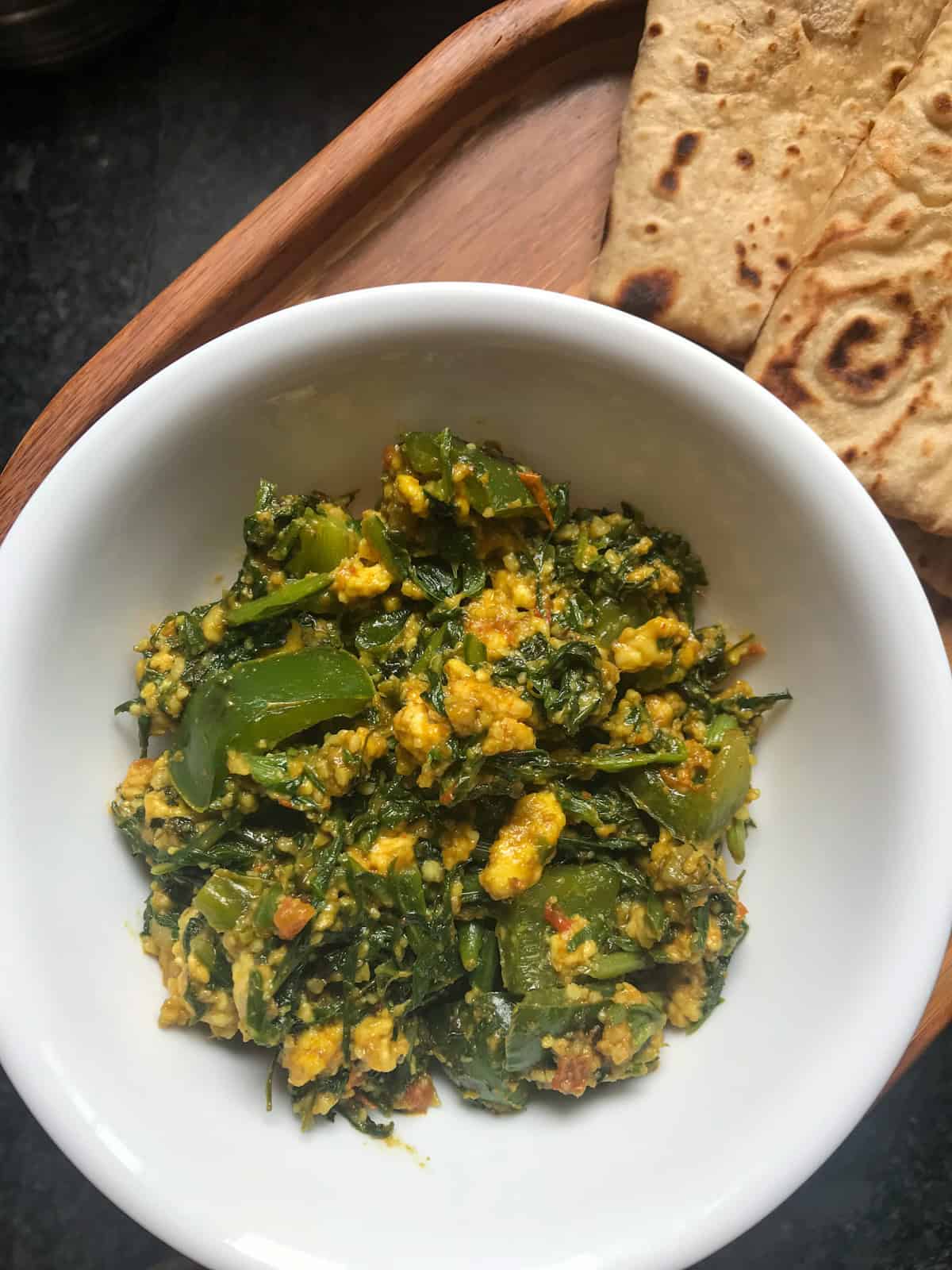Spinach paneer bhurji in a white bowl, served with chapati on a wooden tray for a wholesome Indian meal.