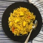 Black plate of paneer vegetable pulao served with spoon on striped cloth.
