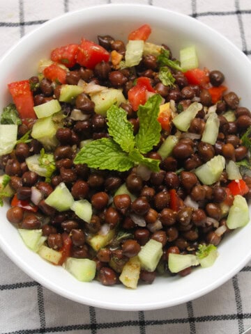 Bowl of Indian kala chana salad with cucumber, tomato, onion, and mint garnish.
