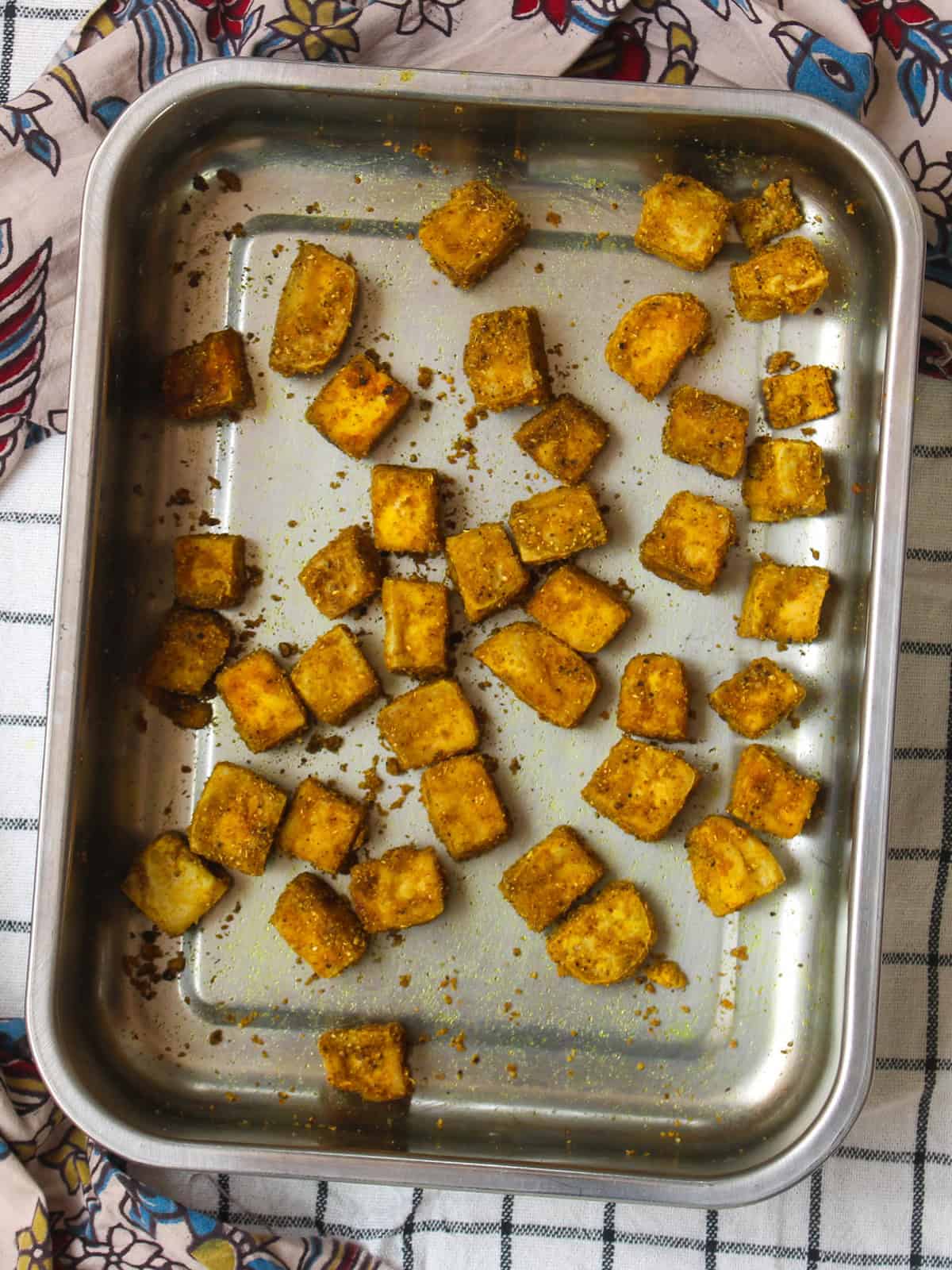 Close-up of roasted tofu cubes coated in Indian spices, baked in a steel tray for a simple protein-rich dish.