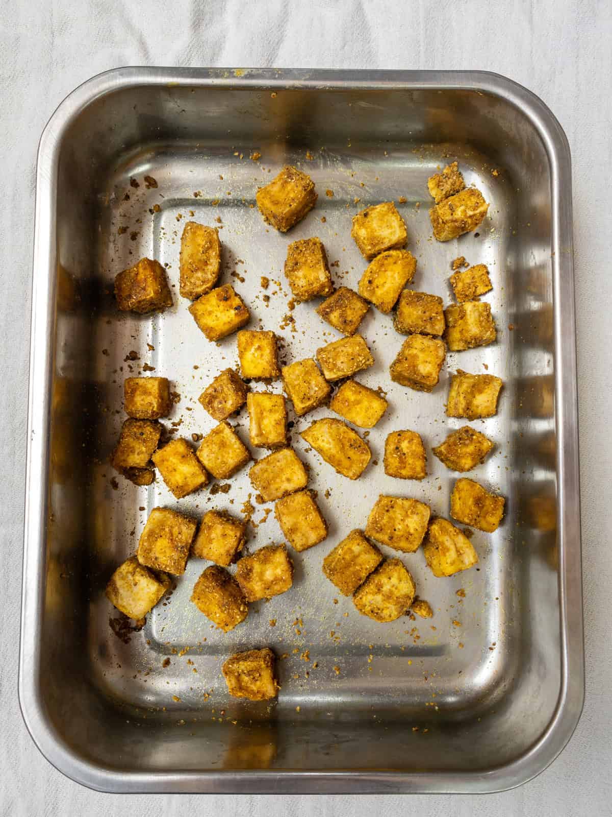 Baked tofu cubes turning golden and crisp after roasting with Indian spices in a steel tray.