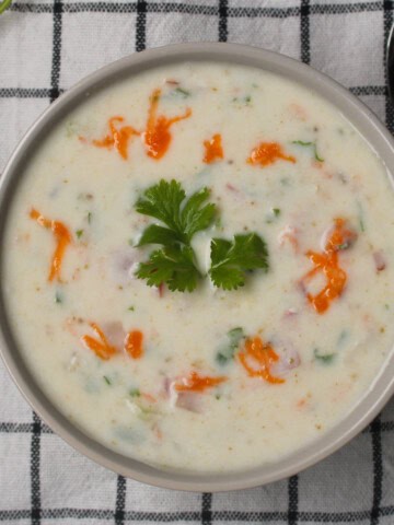 Indian yogurt sauce (raita) served in a bowl, garnished with cilantro and red chili oil, perfect side dish for biryani and pulao.