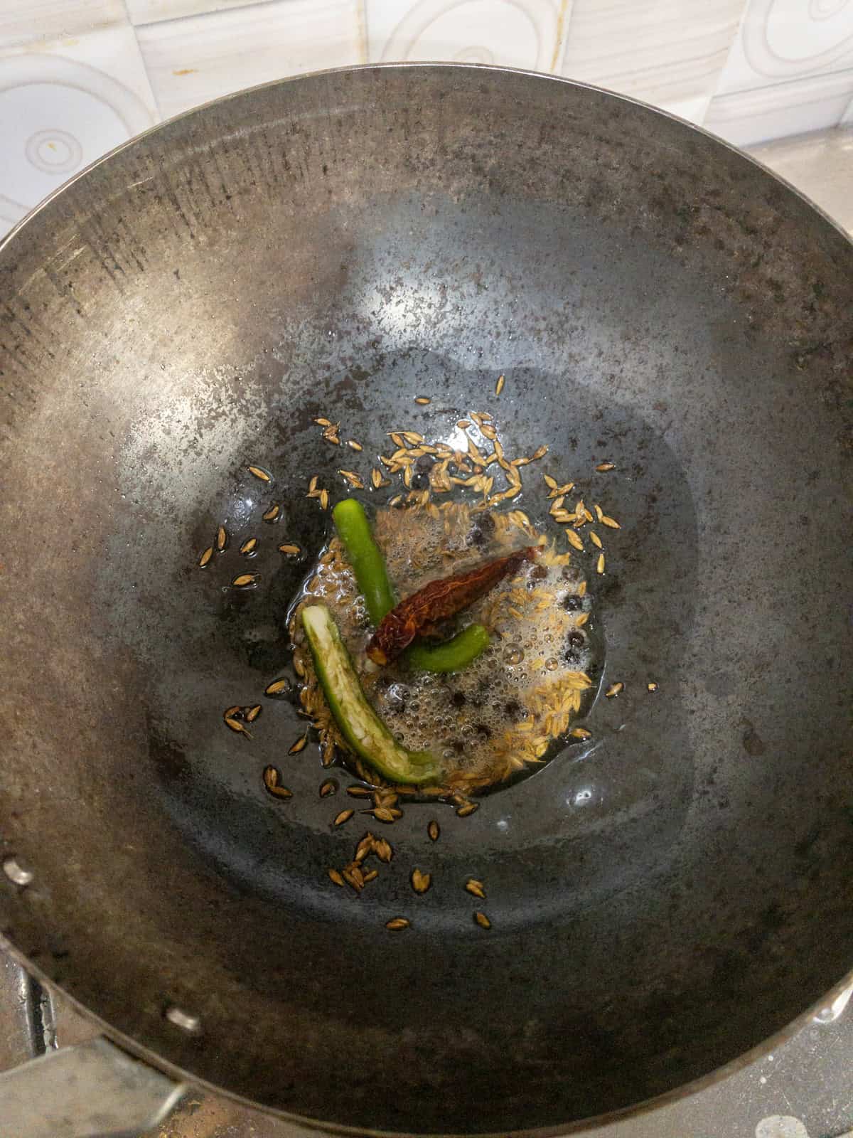 Green chili and dried red chili frying in hot oil with cumin seeds.