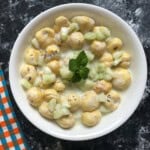 Top view of makhana raita with yogurt, cucumber, and fresh mint leaves in a white bowl on a dark surface.
