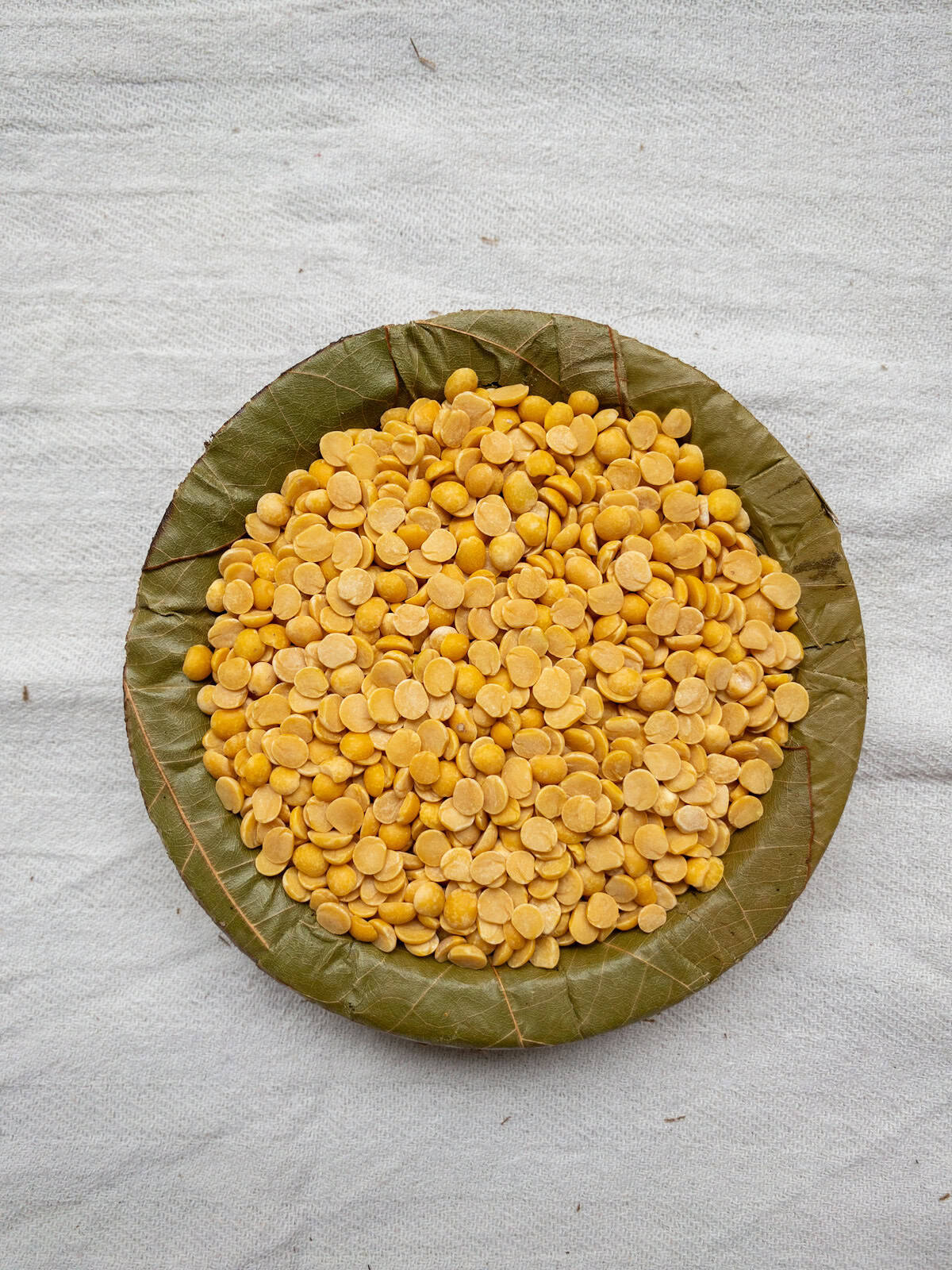 Split pigeon peas (toor dal) in a leaf bowl, showing their medium size and warm golden-yellow tone.