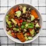 Close-up top view of roasted pumpkin and black chickpea salad with fresh cucumber, tomato, and herbs.