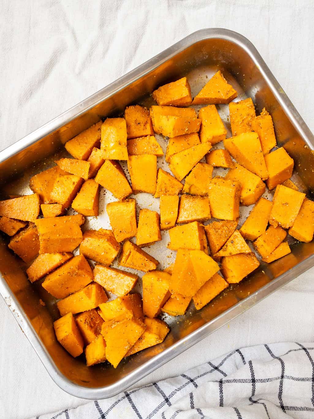 Pumpkin cubes evenly coated with oil and spices, ready to be roasted for the salad.