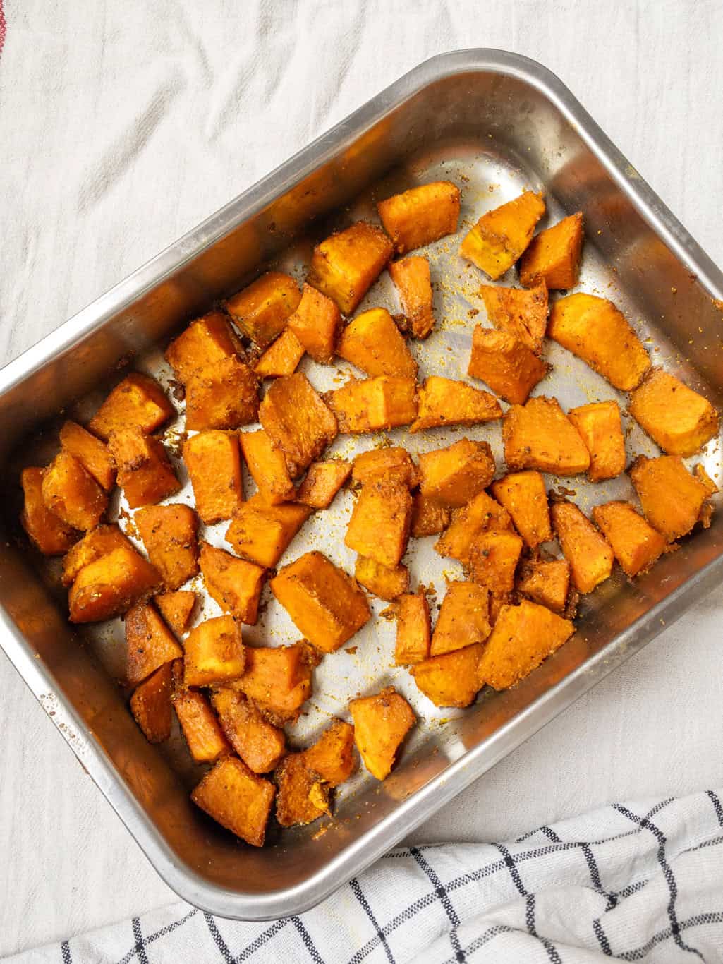 Golden brown roasted pumpkin cubes in a baking tray after baking until tender and caramelized.