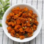 Close-up of Indian style pumpkin stir fry with tender orange pumpkin cubes sautéed with onions and spices, served in a white bowl.
