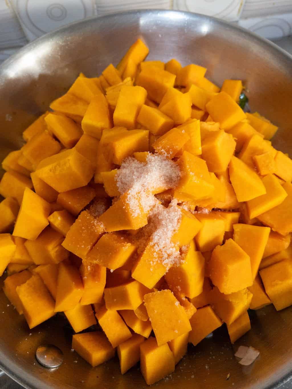 Fresh orange pumpkin cubes with salt added to the sautéed onion mixture in a pan for kaddu sabzi preparation.
